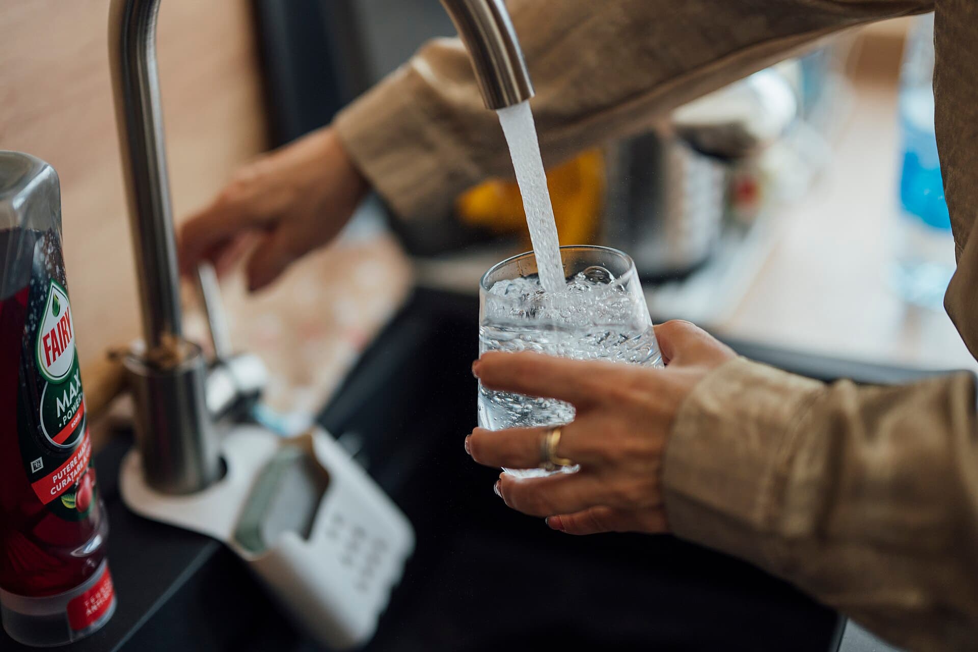 A person fills a glass with water at a kitchen sink